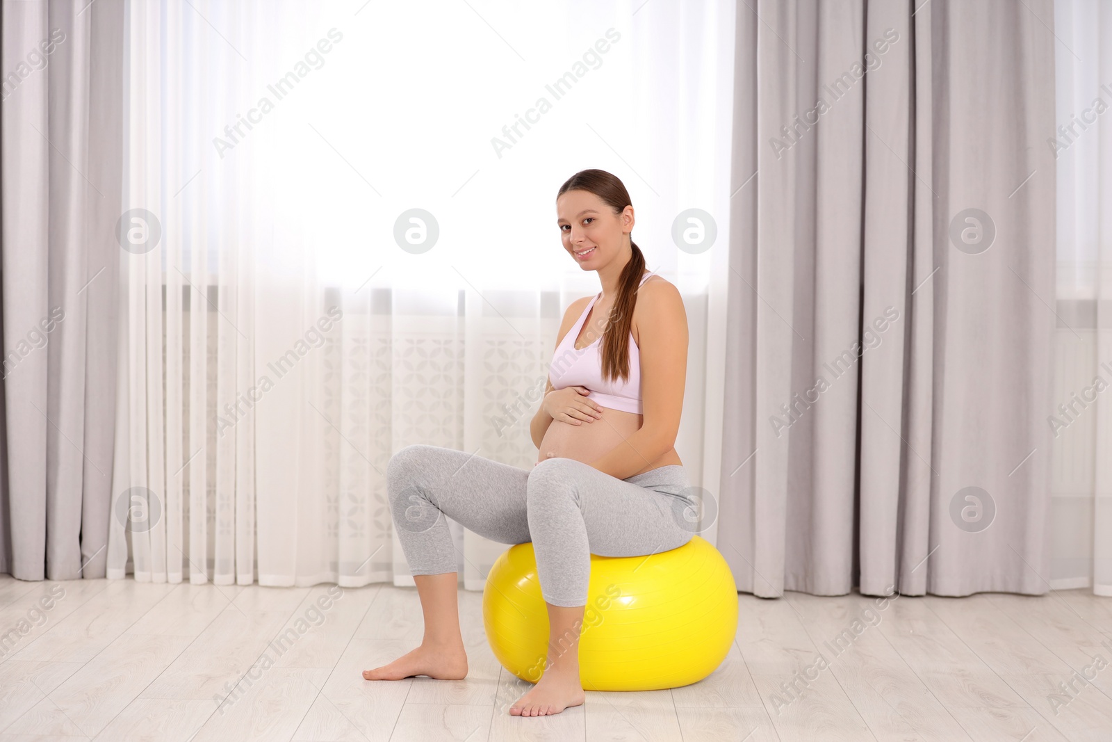 Photo of Pregnant woman sitting on fitness ball at home. Doing yoga