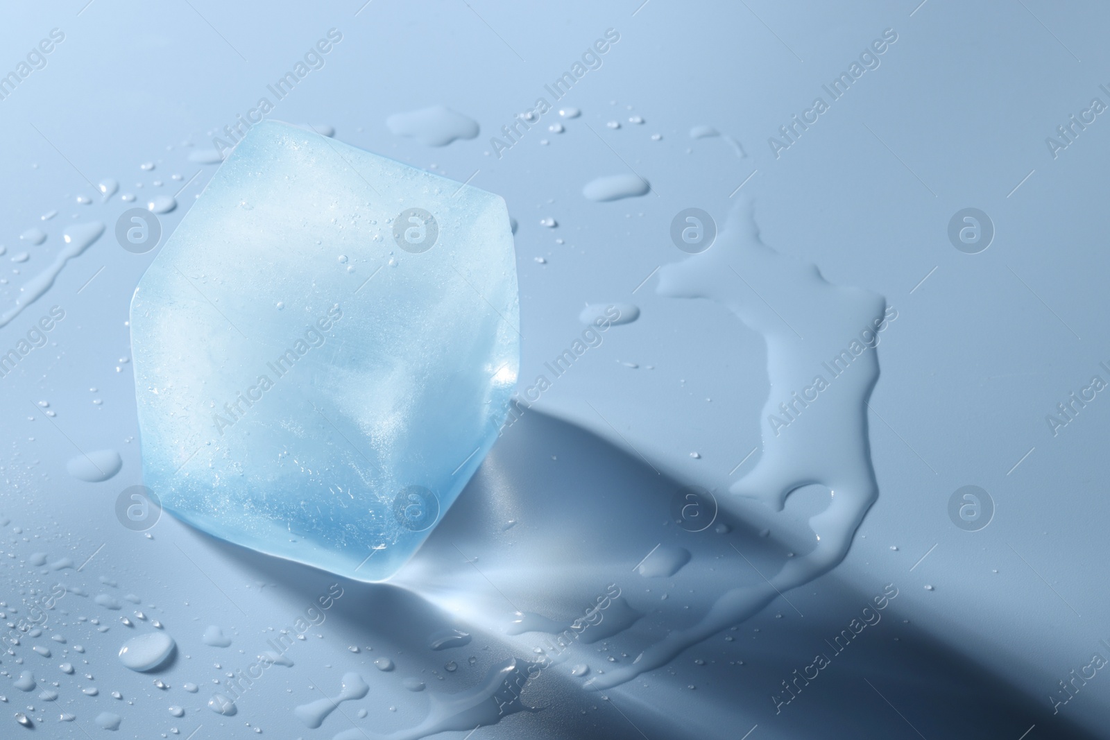 Photo of Crystal clear ice cube on light blue background, space for text