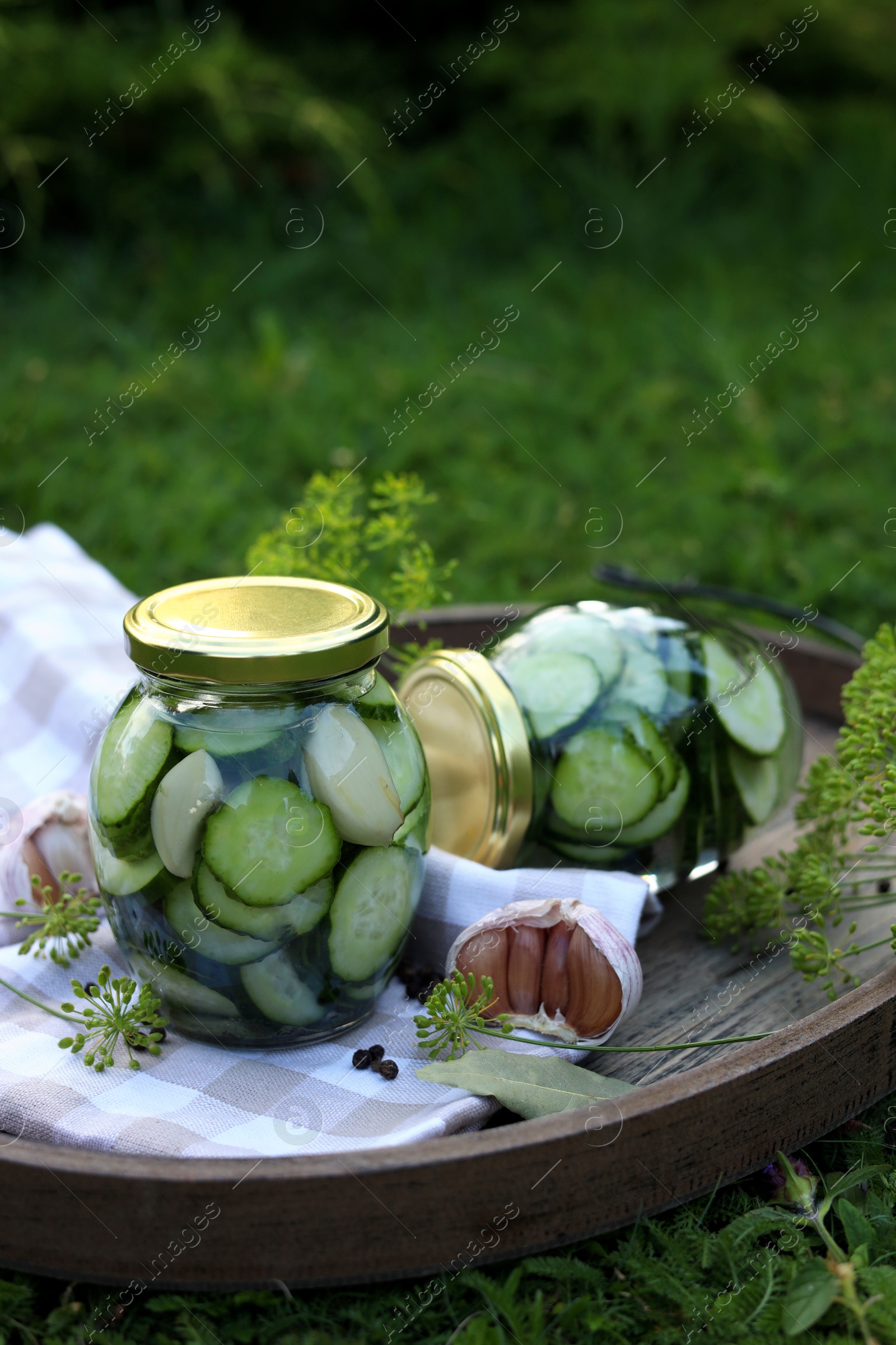 Photo of Jar of delicious pickled cucumbers on wooden tray outdoors