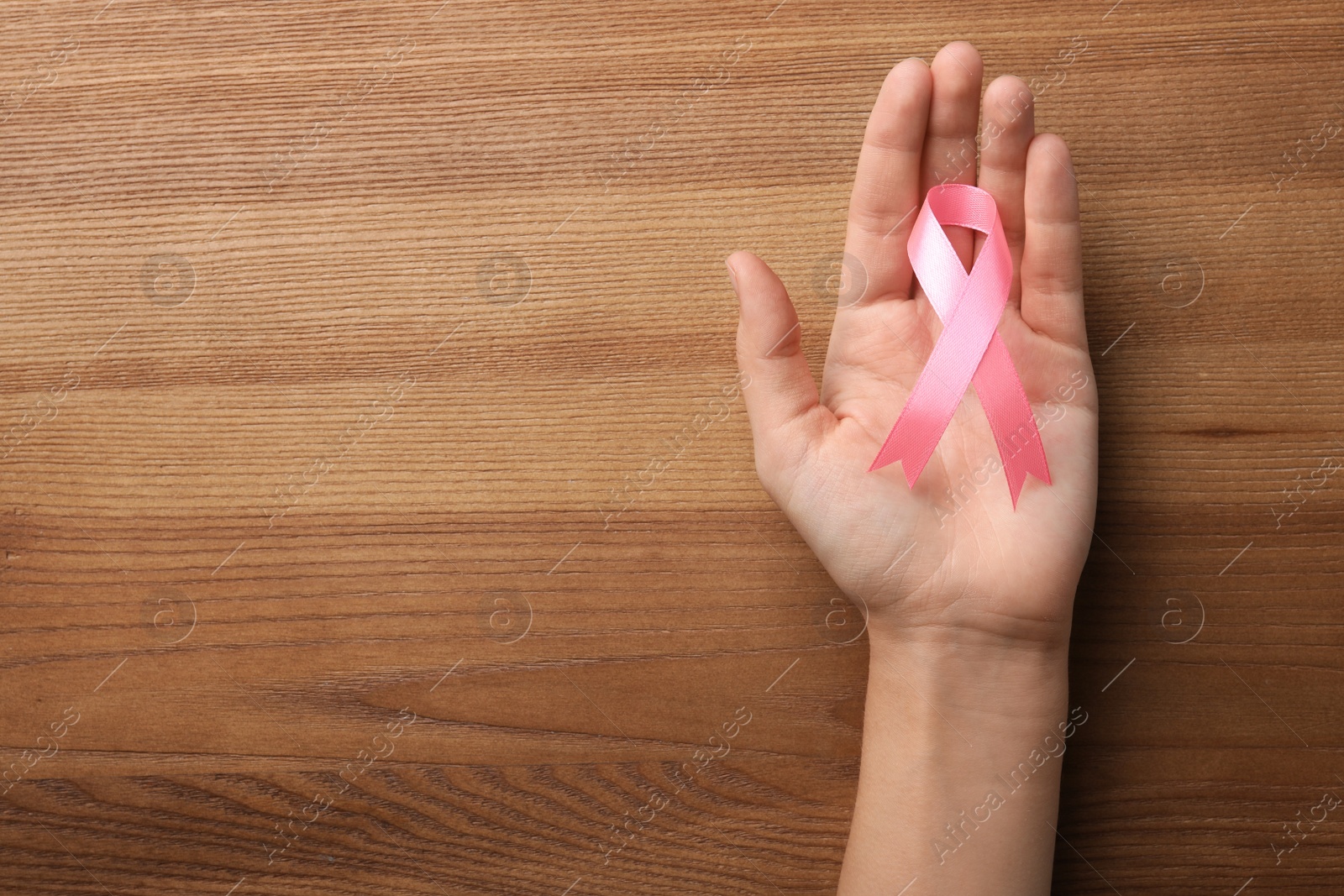 Photo of Woman holding pink ribbon on wooden background, top view with space for text. Breast cancer awareness concept