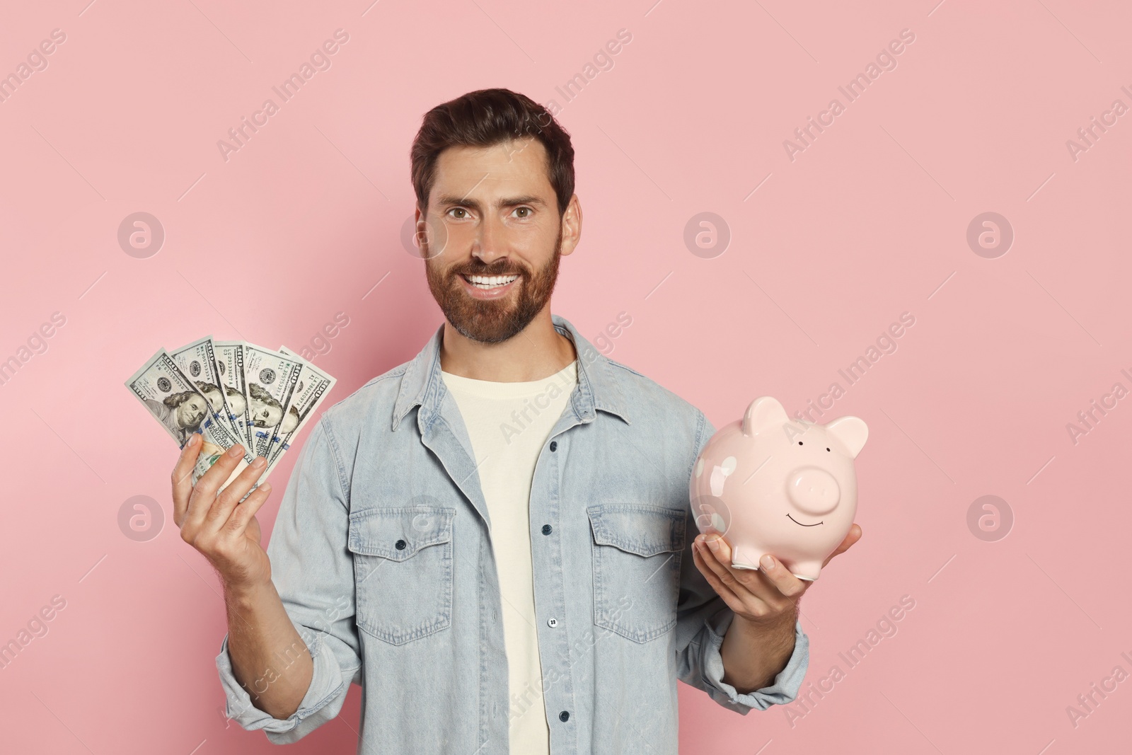 Photo of Happy man with money and piggy bank on pale pink background