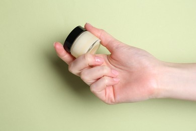 Woman holding jar of cream on green background, closeup