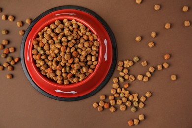 Dry dog food and feeding bowl on brown background, flat lay