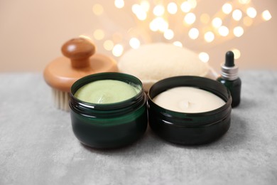 Photo of Natural scrub and other body care products on grey table against blurred lights