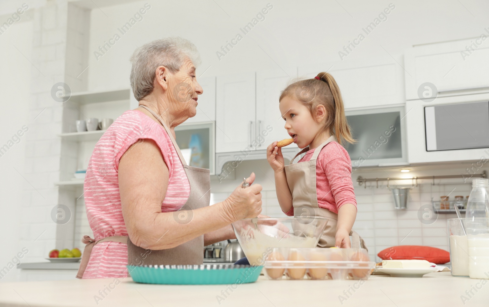 Photo of Cute girl and her grandmother cooking in kitchen