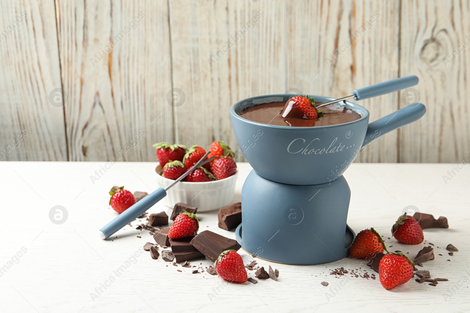 Photo of Fondue pot with chocolate and fresh strawberries on white table