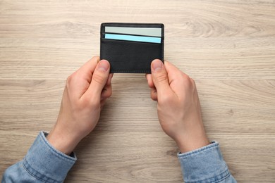 Man holding leather business card holder with cards at wooden table, top view