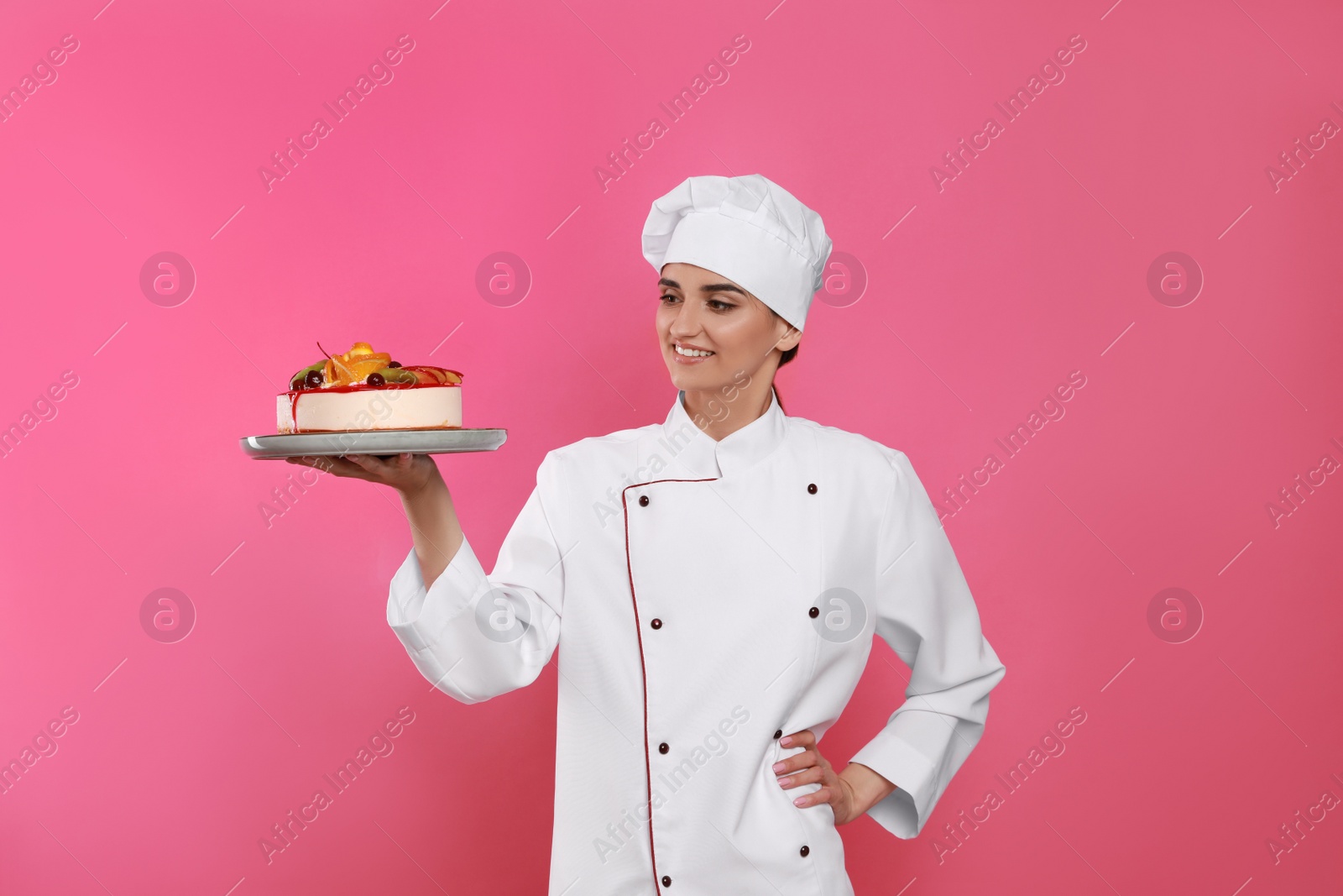 Photo of Happy professional confectioner in uniform holding delicious cake on pink background