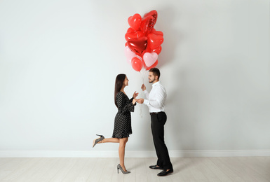 Photo of Happy young couple with heart shaped balloons near light wall. Valentine's day celebration