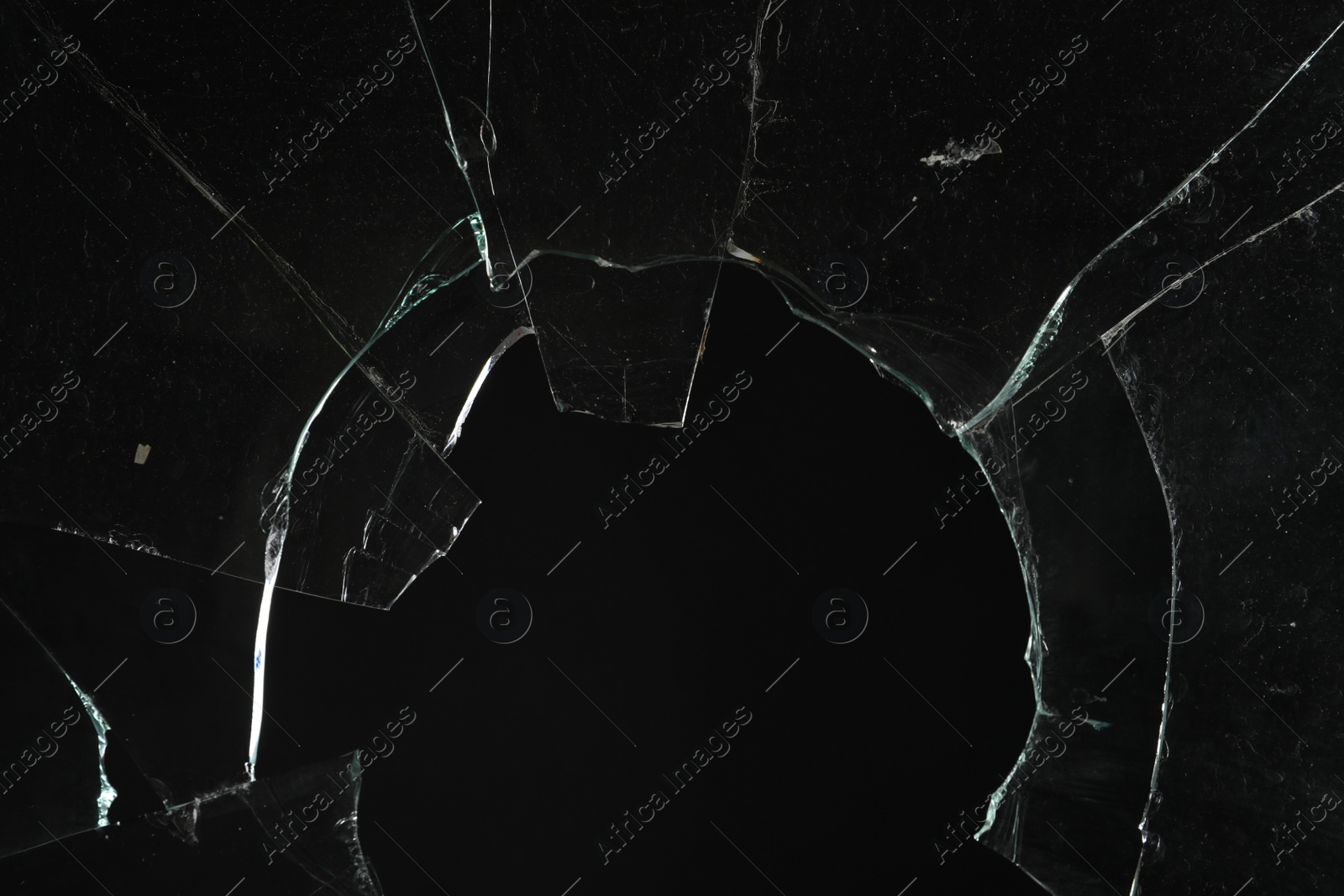 Photo of Closeup view of broken glass with cracks on black background