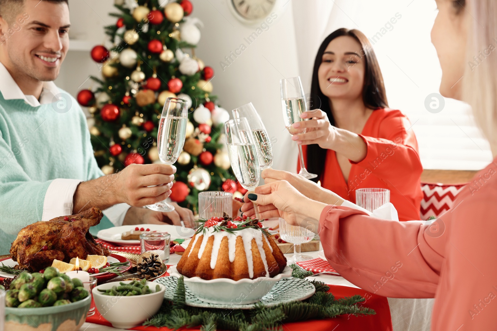 Photo of Happy friends clinking glasses of sparkling wine at festive dinner indoors. Christmas Eve celebration