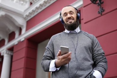 Mature man with headphones listening to music outdoors. Space for text