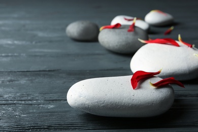 Spa stones and flower petals on wooden table, closeup. Space for text