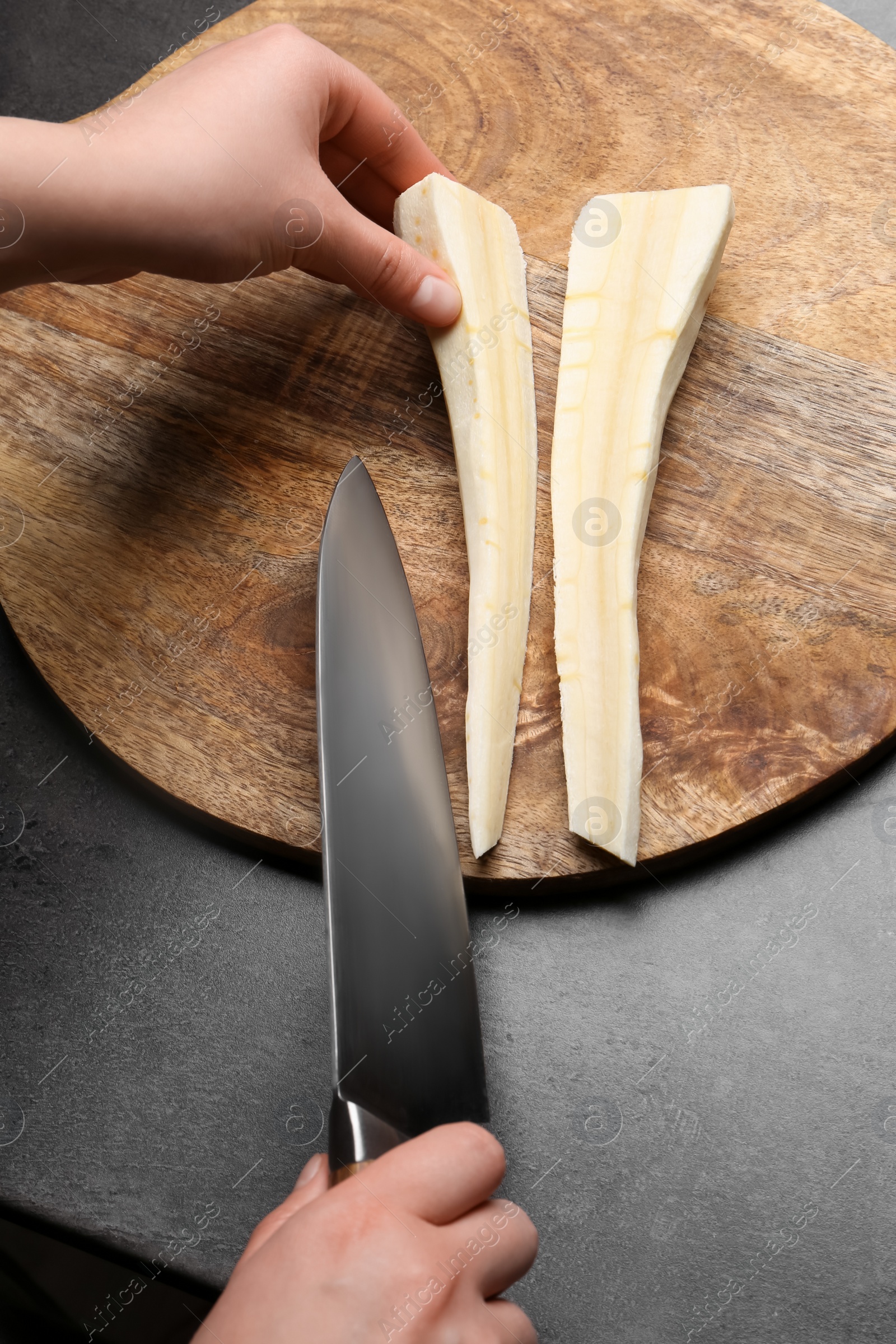 Photo of Woman cutting delicious fresh ripe parsnip at black table, top view