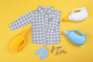 Photo of Flat lay composition with detergents and children's clothes on yellow background