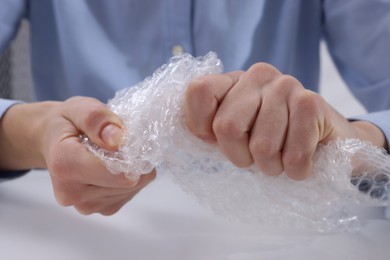 Photo of Woman popping bubble wrap at table in office, closeup. Stress relief