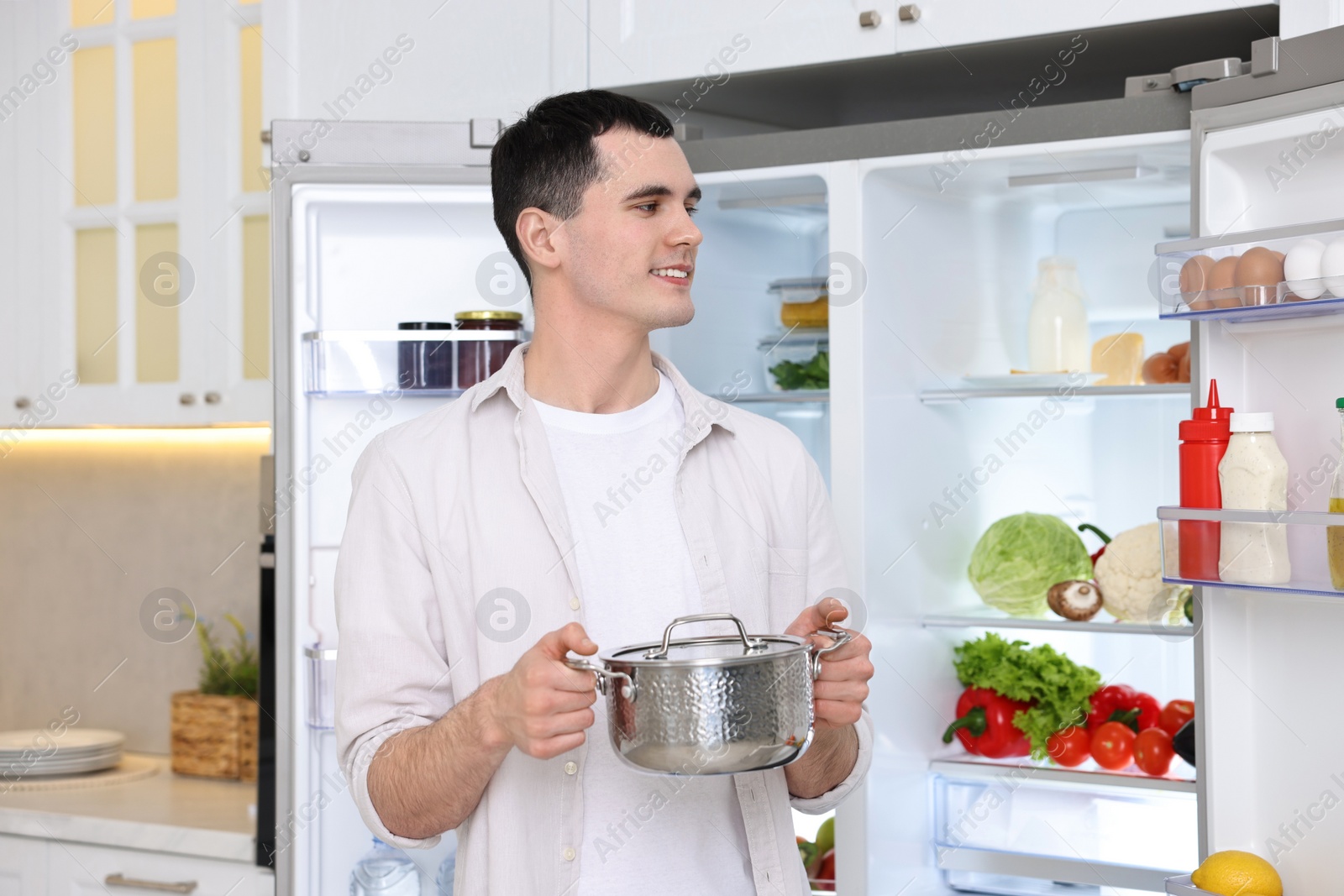 Photo of Happy man holding pot near refrigerator in kitchen