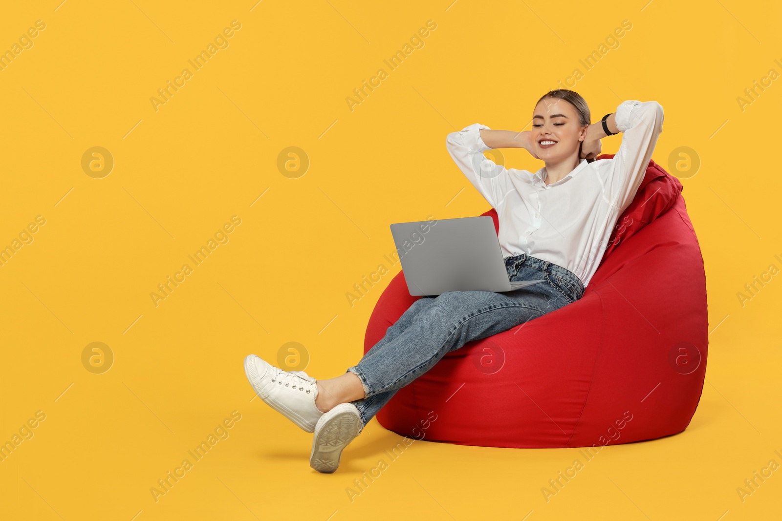 Photo of Happy woman with laptop sitting on beanbag chair against orange background. Space for text