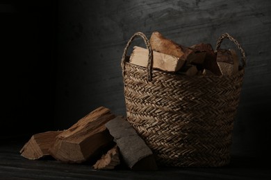 Photo of Wicker basket with cut firewood on black table