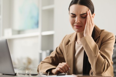 Woman suffering from headache at workplace in office, space for text