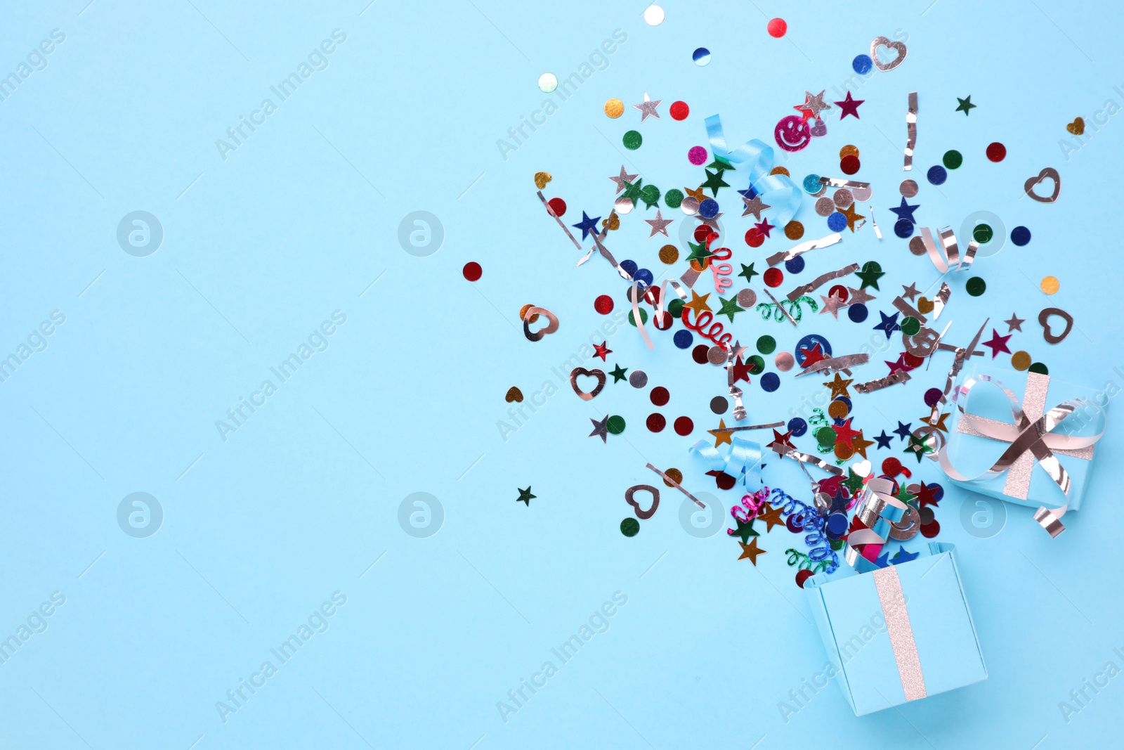 Photo of Colorful confetti and box on light blue background, top view. Space for text