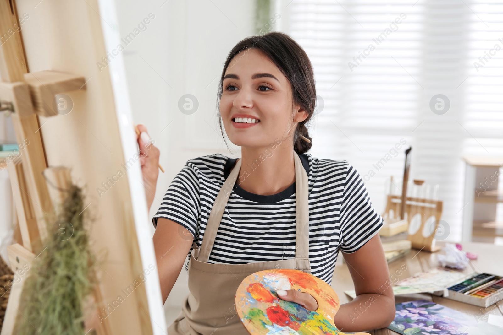 Photo of Young woman drawing on easel with brush, closeup