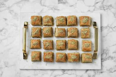 Photo of Delicious fresh baklava with chopped nuts on white marble table, top view. Eastern sweets