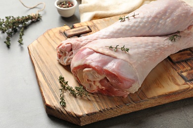 Photo of Board with raw turkey drumsticks, spices and thyme on table, closeup