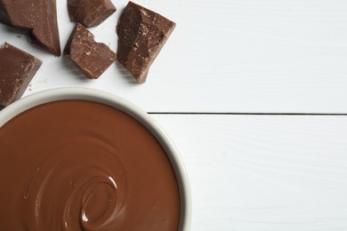 Tasty milk chocolate paste in bowl and pieces on white wooden table, flat lay. Space for text