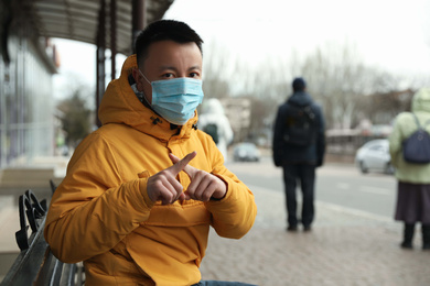 Asian man wearing medical mask on city street, space for text. Virus outbreak