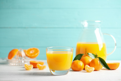 Glass of fresh tangerine juice and fruits on white wooden table