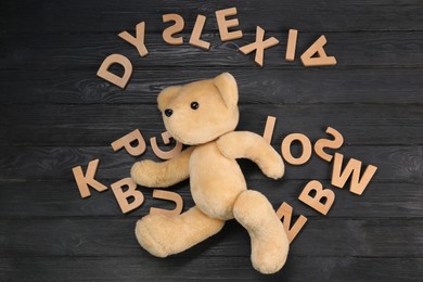 Photo of Word Dyslexia made of letters and teddy bear on dark wooden table, flat lay