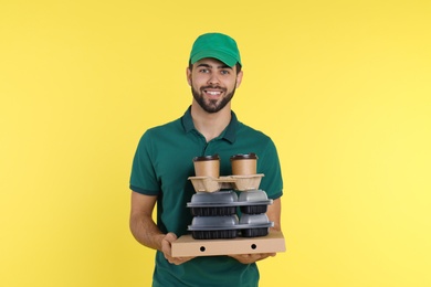 Young courier with different orders on color background. Food delivery service