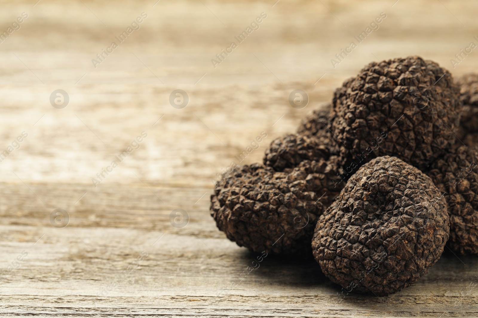 Photo of Heap of black truffles on wooden table, closeup. space for text