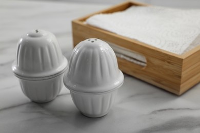 Photo of Ceramic salt and pepper shakers near box of napkins on white marble table in kitchen. Space for text