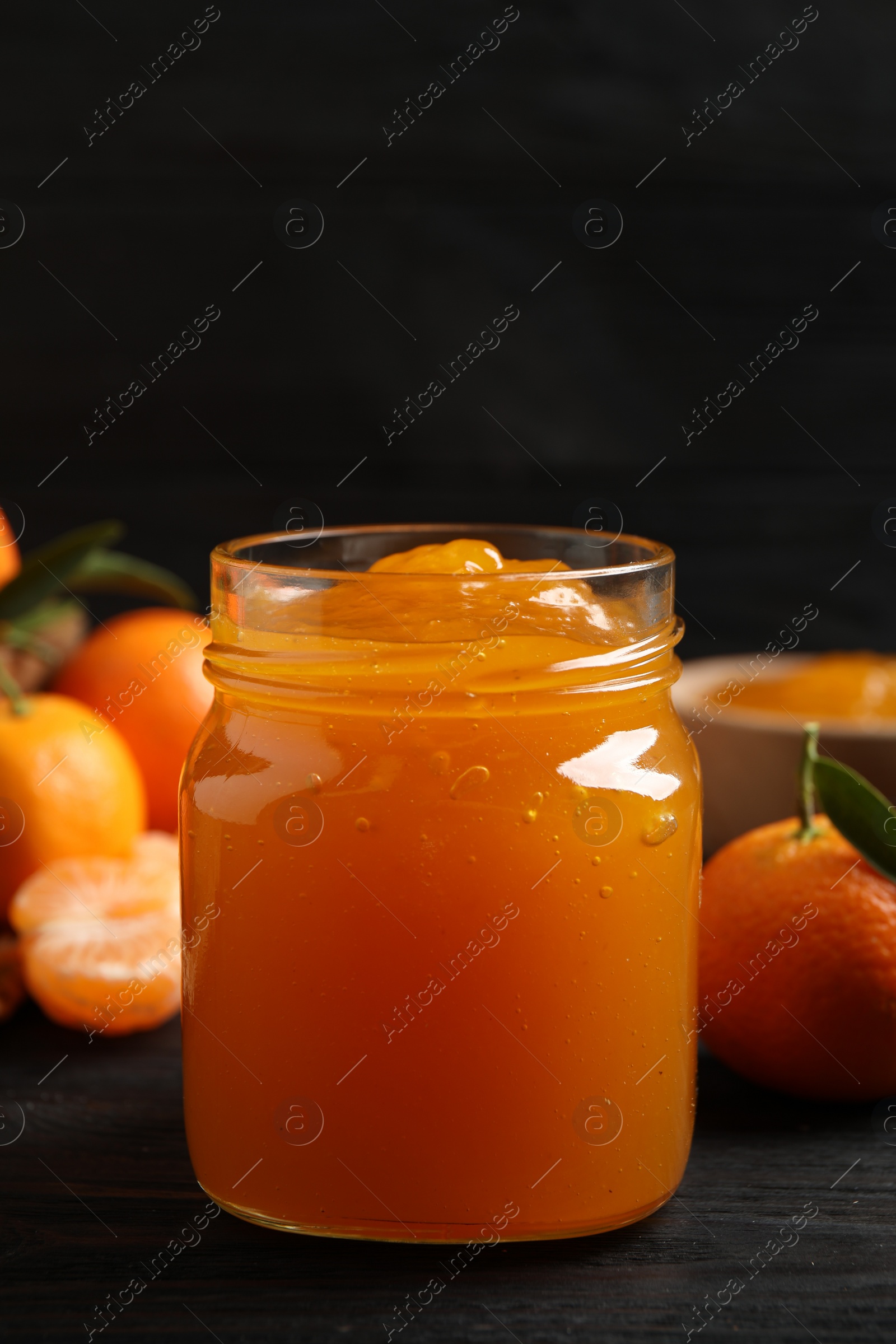 Photo of Tasty tangerine jam in glass jar on dark wooden table. Space for text