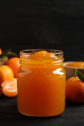 Tasty tangerine jam in glass jar on dark wooden table. Space for text