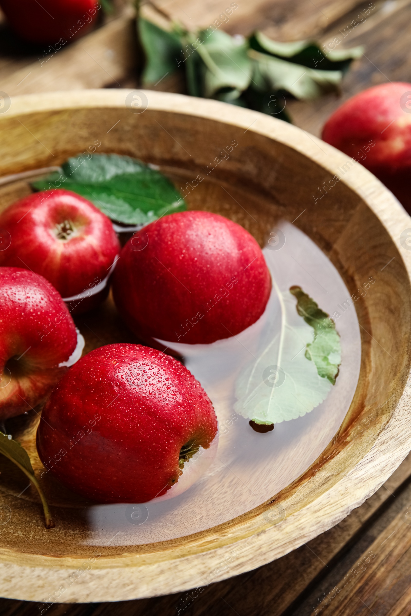 Photo of Ripe red apples in bowl of water on wooden table, closeup