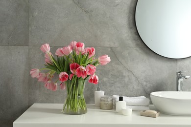 Vase with beautiful pink tulips and toiletries near sink in bathroom