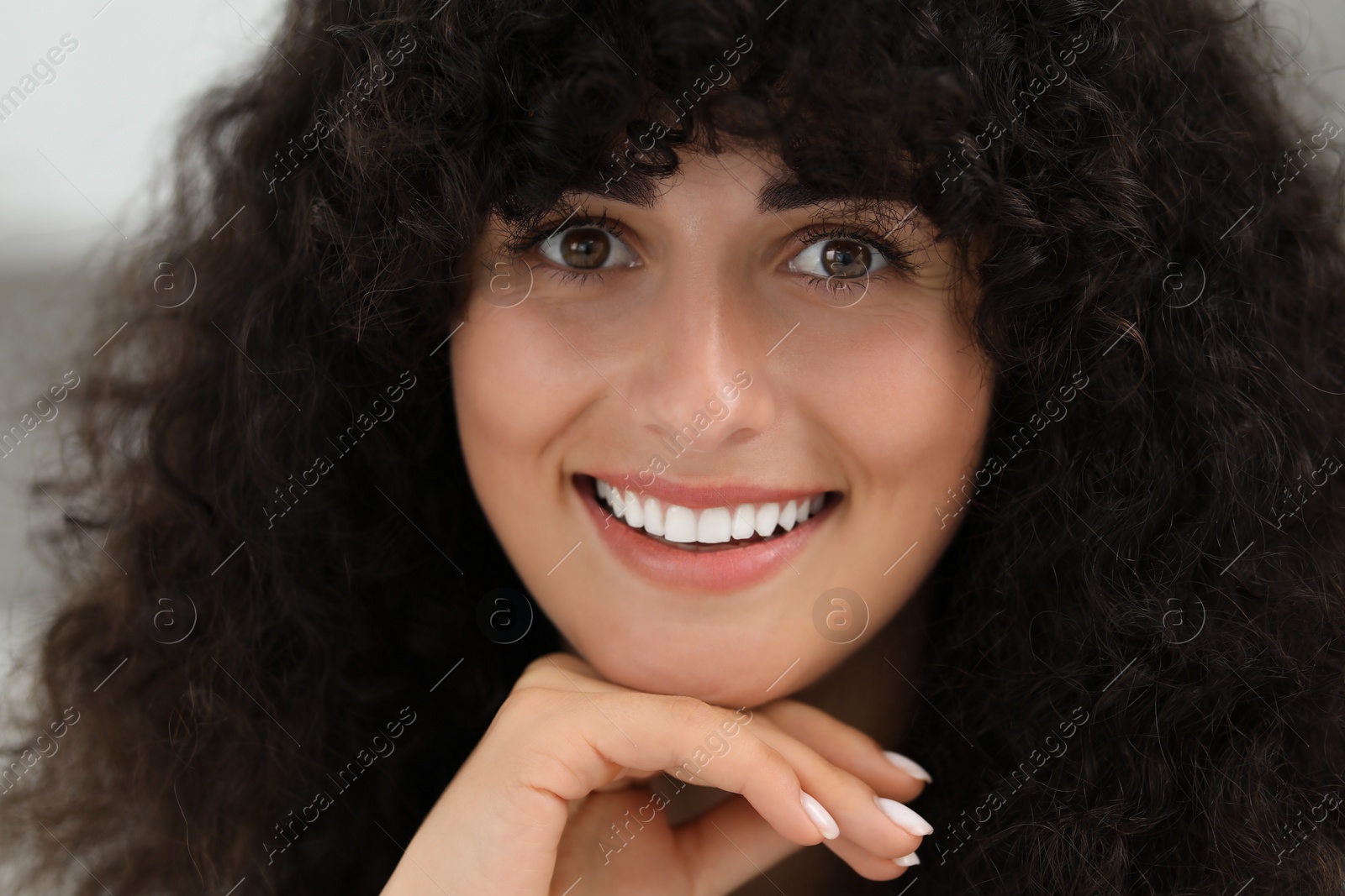 Photo of Portrait of beautiful woman with curly hair on blurred background. Attractive lady smiling and looking into camera