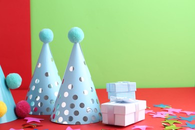 Party hats and gift boxes on color background, space for text