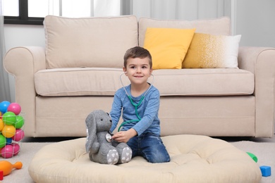 Photo of Cute child playing doctor with stuffed toy on floor in hospital