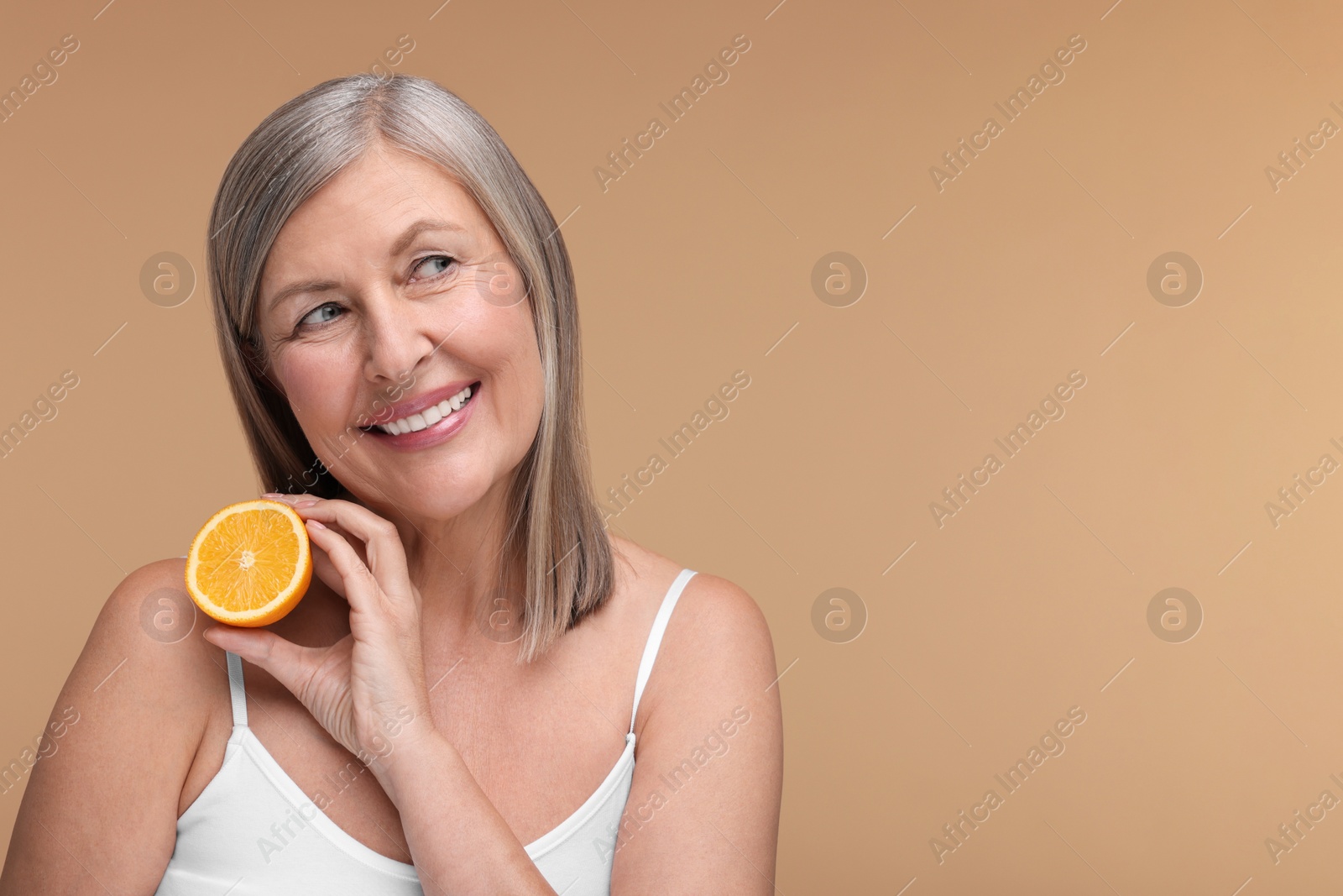 Photo of Beautiful woman with half of orange rich in vitamin C on beige background, space for text