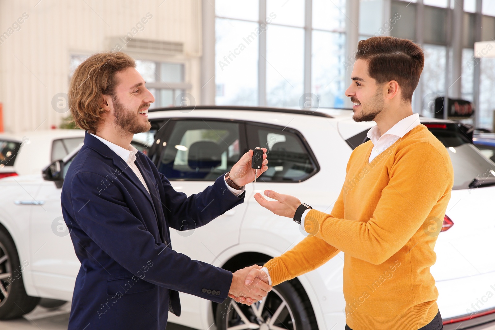 Photo of Car salesman giving key to customer while shaking hands in dealership