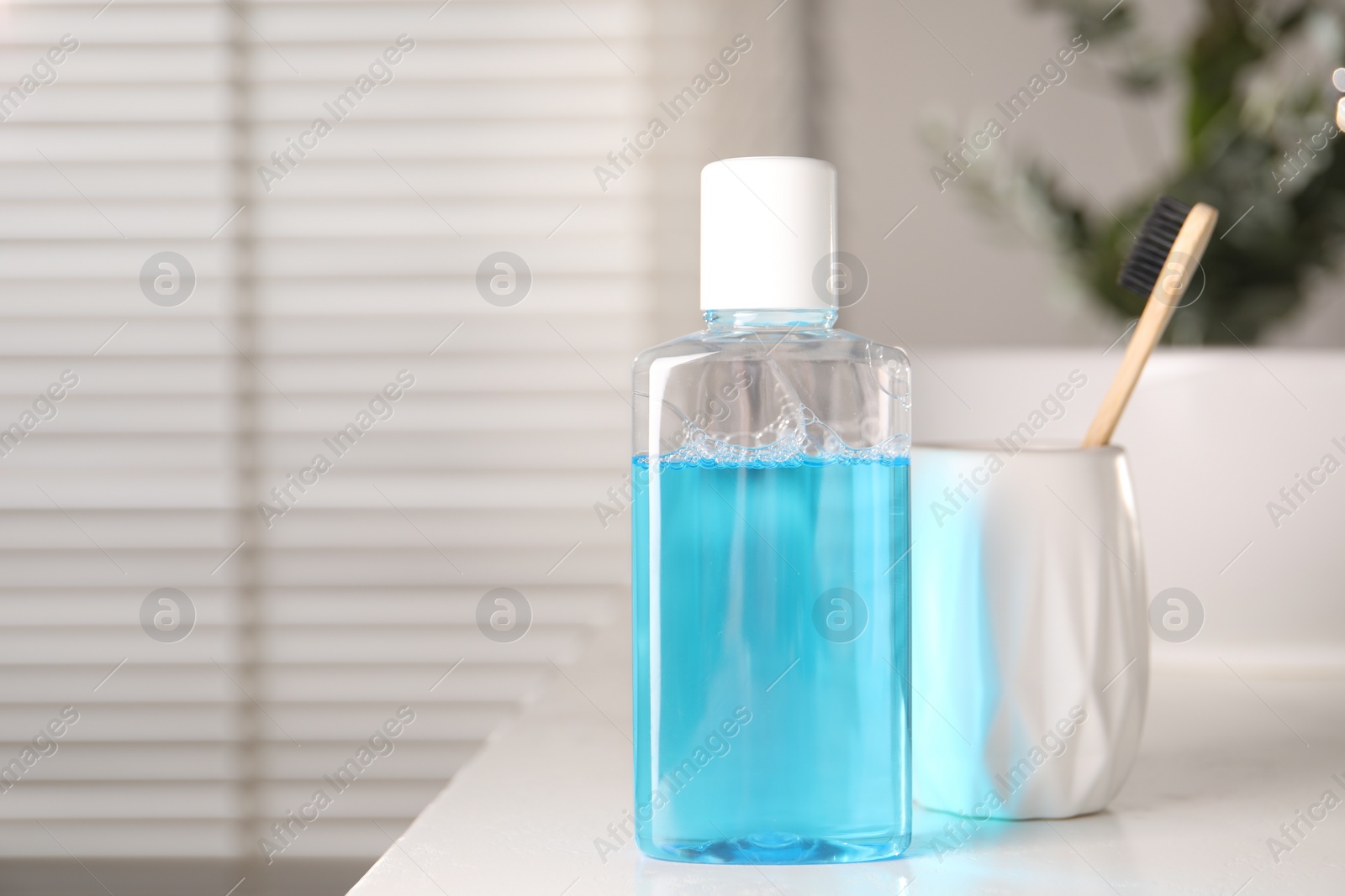 Photo of Bottle of mouthwash and toothbrush on white countertop in bathroom, space for text