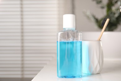 Photo of Bottle of mouthwash and toothbrush on white countertop in bathroom, space for text