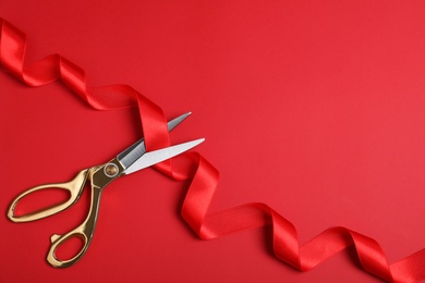 Photo of Stylish scissors and red ribbon on color background, flat lay with space for text. Ceremonial tape cutting