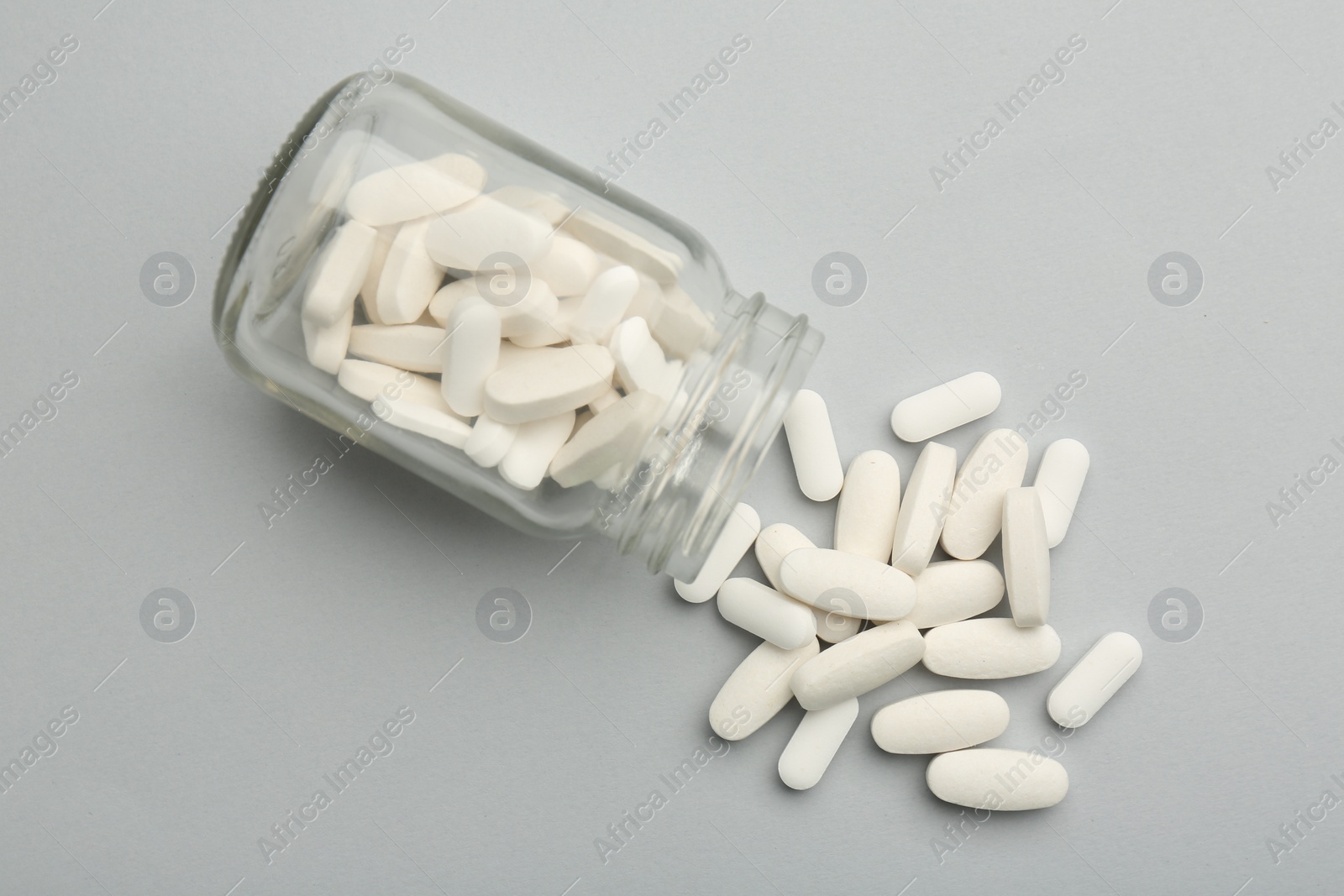 Photo of Vitamin pills and bottle on grey background, top view