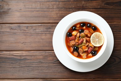 Photo of Meat solyanka soup with sausages, olives and vegetables on wooden table, top view. Space for text