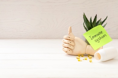 Photo of Mannequin hand, pills and note with phrase Immune System on white wooden table. Space for text